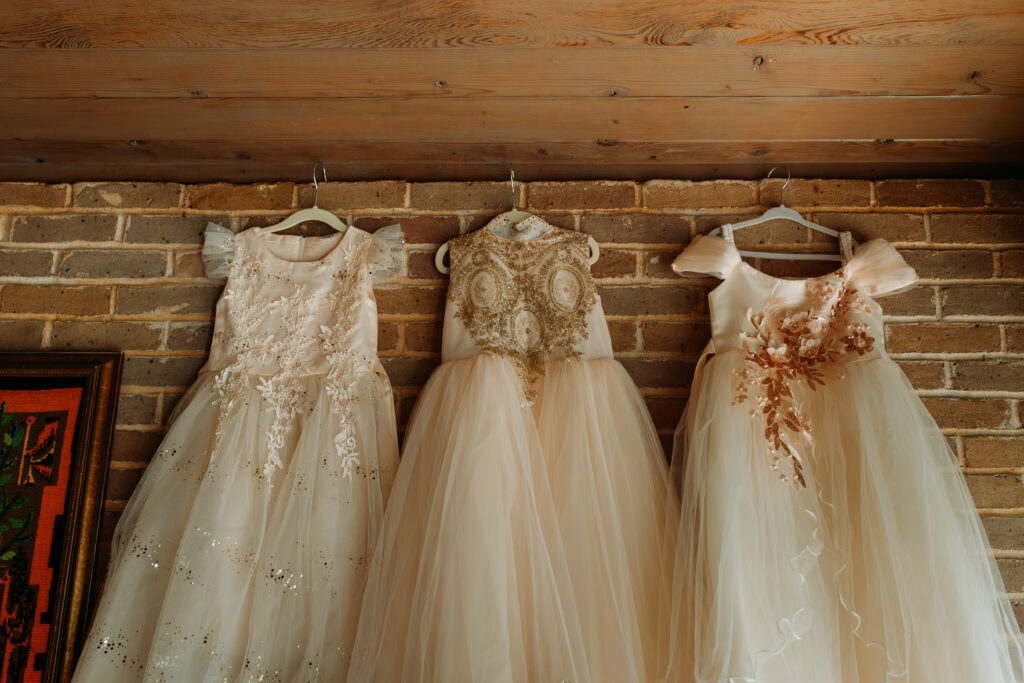 Brides daughters white dresses on hangers on brick wall.