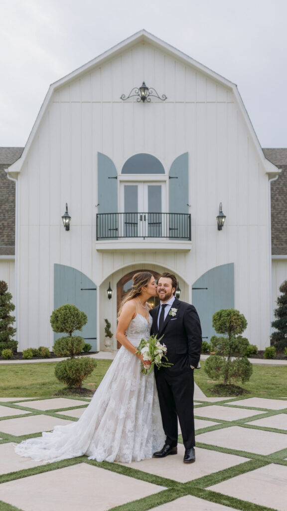 Couple (Bride in gown and Groom in tux) kiss in front ofThe French Farmhouse in Collinsville Texas