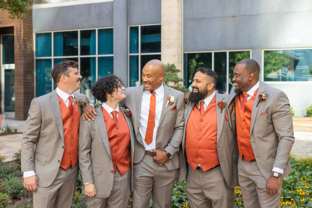 Groom and his grooms party laugh and joke while huddled together 