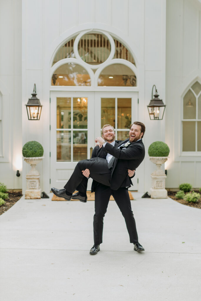 Grooms man picks up Groom and laugh while in front of the Chapel at The French Farmhouse in DFW
