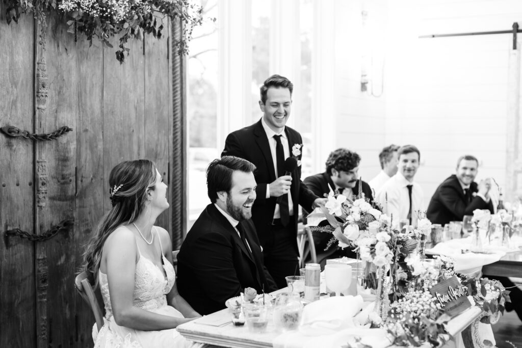 Groomsman and wedding couple laughing during toast at The French Farmhouse