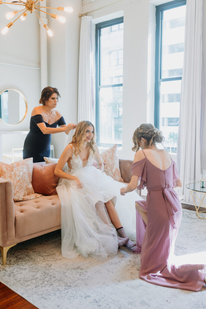 Bride sitting and getting ready with assistance from mother of bride and bridesmaid at The Century Hall Bridal suite
